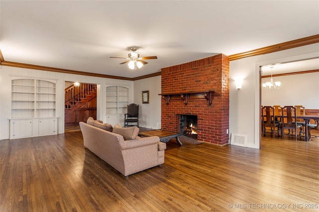 living room featuring hardwood / wood-style flooring, built in shelves, crown molding, ceiling fan with notable chandelier, and a fireplace