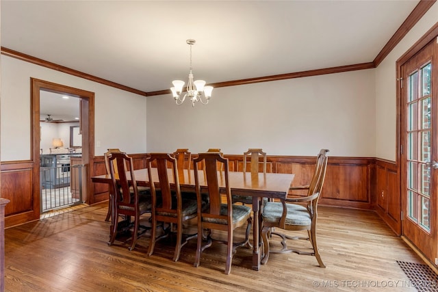 dining area with ornamental molding, light wood-type flooring, and ceiling fan with notable chandelier