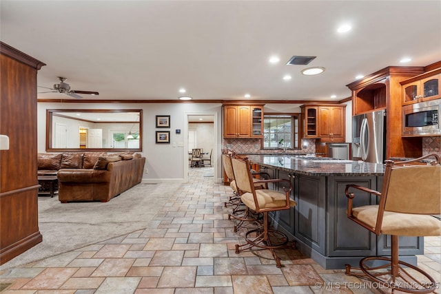 kitchen featuring stainless steel appliances, ceiling fan, decorative backsplash, a wealth of natural light, and a breakfast bar