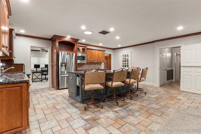 kitchen with dark stone countertops, a breakfast bar area, decorative backsplash, a center island with sink, and appliances with stainless steel finishes