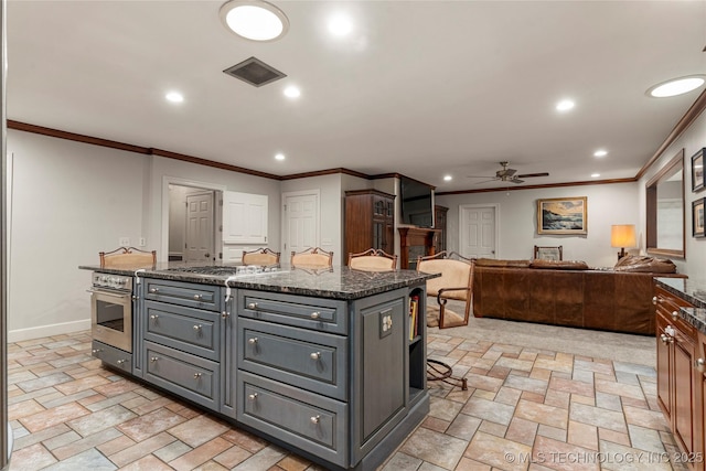 kitchen with a kitchen island with sink, gray cabinetry, ceiling fan, dark stone counters, and ornamental molding