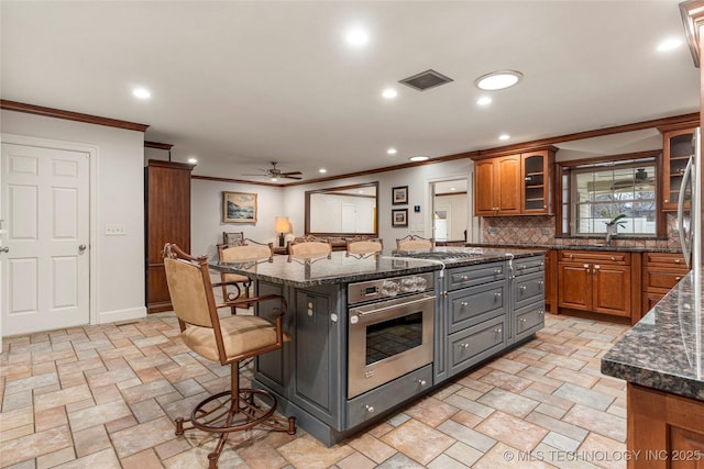 kitchen featuring ceiling fan, an island with sink, dark stone counters, a breakfast bar, and appliances with stainless steel finishes