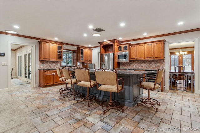 kitchen with a chandelier, stainless steel appliances, an island with sink, decorative backsplash, and a kitchen breakfast bar