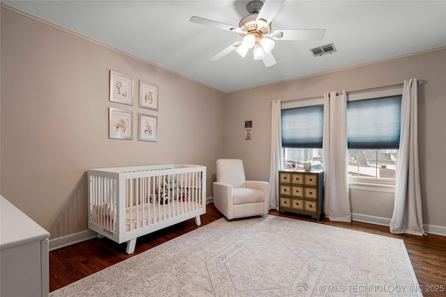 unfurnished bedroom featuring a nursery area, ceiling fan, and dark wood-type flooring