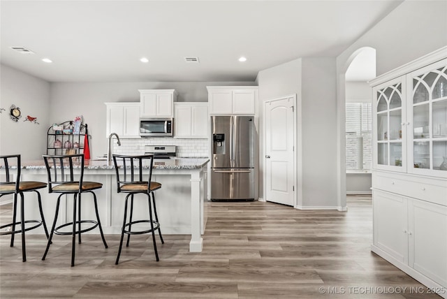 kitchen featuring appliances with stainless steel finishes, white cabinetry, a kitchen island with sink, and light stone counters