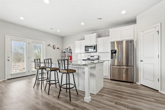 kitchen featuring white cabinets, appliances with stainless steel finishes, wood-type flooring, and a kitchen island with sink