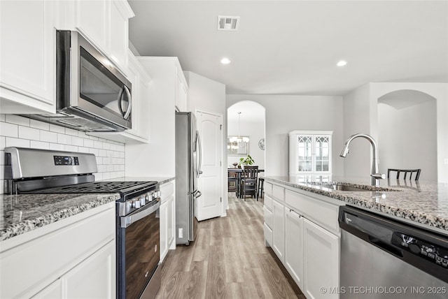 kitchen with appliances with stainless steel finishes, sink, light stone counters, white cabinets, and tasteful backsplash