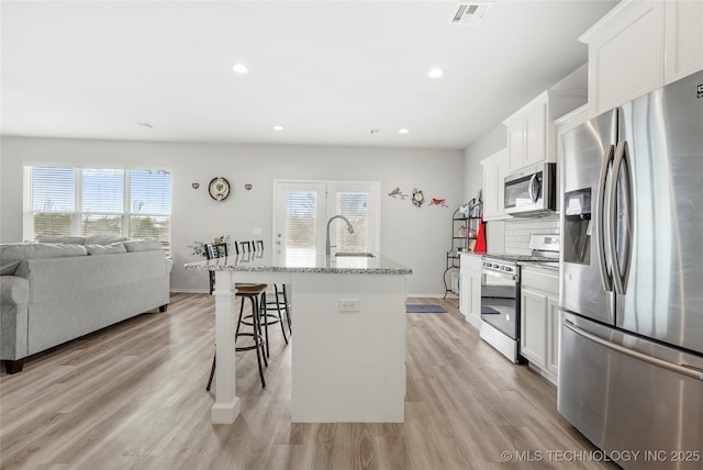 kitchen with white cabinetry, a kitchen breakfast bar, light hardwood / wood-style flooring, a center island with sink, and appliances with stainless steel finishes