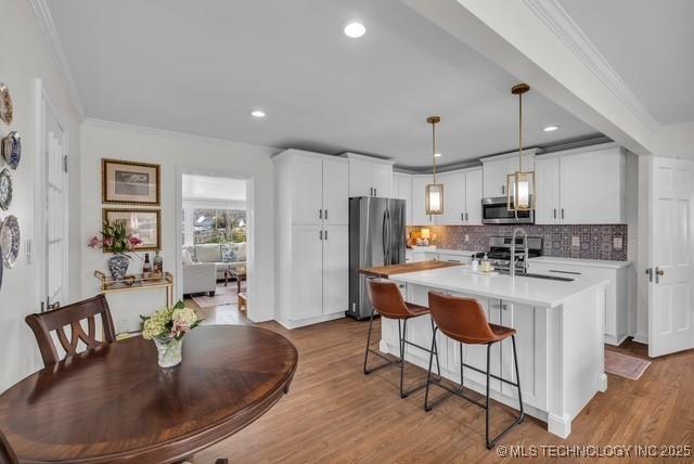 kitchen with stainless steel appliances, sink, white cabinets, light hardwood / wood-style flooring, and pendant lighting