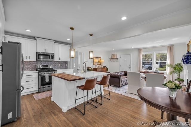 kitchen featuring white cabinets, tasteful backsplash, hanging light fixtures, a center island with sink, and appliances with stainless steel finishes