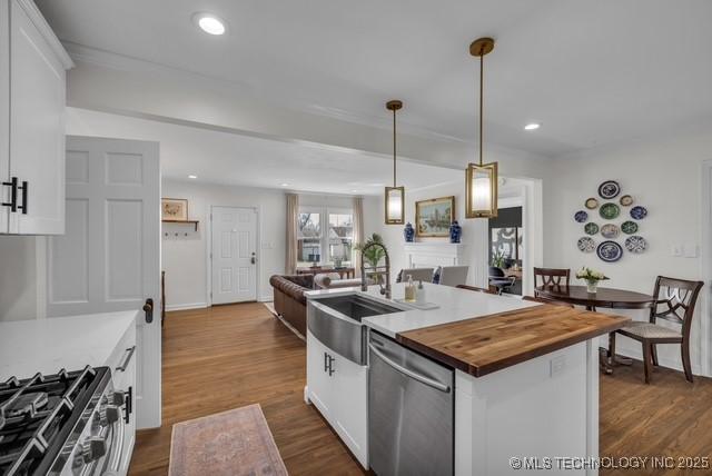 kitchen featuring stainless steel appliances, white cabinetry, an island with sink, butcher block countertops, and hanging light fixtures