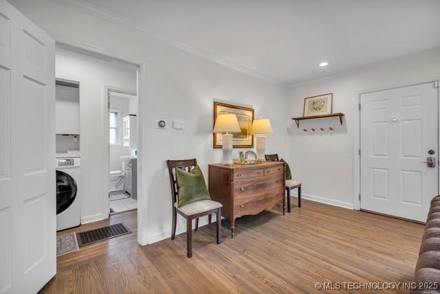 living area featuring washer / clothes dryer, ornamental molding, and light hardwood / wood-style flooring