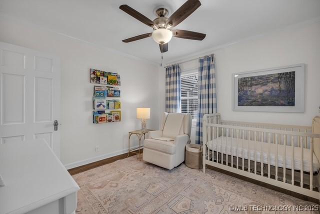 bedroom featuring ceiling fan, crown molding, hardwood / wood-style flooring, and a nursery area