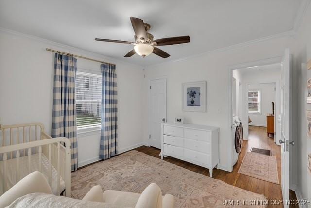 bedroom featuring a crib, washer / dryer, ceiling fan, ornamental molding, and wood-type flooring