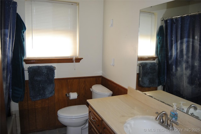 bathroom featuring toilet, wooden walls, a wealth of natural light, and vanity