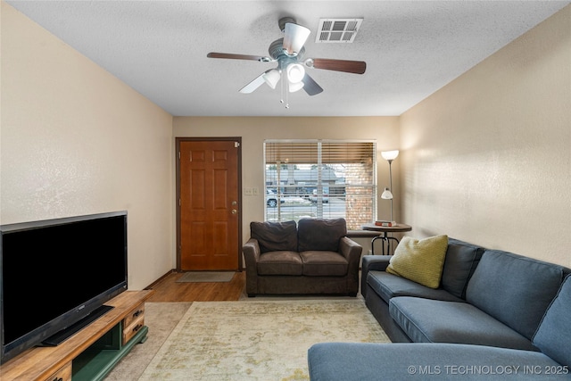 living room with a textured ceiling, ceiling fan, and light hardwood / wood-style flooring