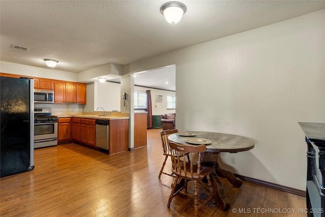 kitchen with stainless steel appliances, a textured ceiling, light hardwood / wood-style flooring, and sink