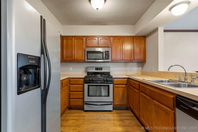 kitchen featuring sink, stainless steel appliances, light wood-type flooring, and a textured ceiling