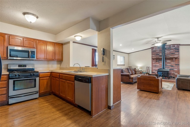 kitchen with light hardwood / wood-style flooring, a wood stove, appliances with stainless steel finishes, ceiling fan, and sink