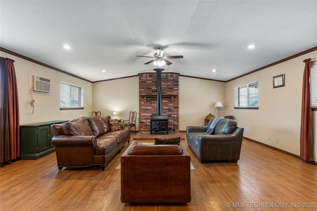 living room featuring a wall unit AC, ceiling fan, a wood stove, hardwood / wood-style flooring, and a textured ceiling