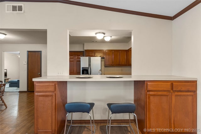 kitchen with kitchen peninsula, stainless steel fridge, dark wood-type flooring, a kitchen bar, and lofted ceiling