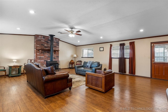 living room with wood-type flooring, ceiling fan, crown molding, and a wood stove