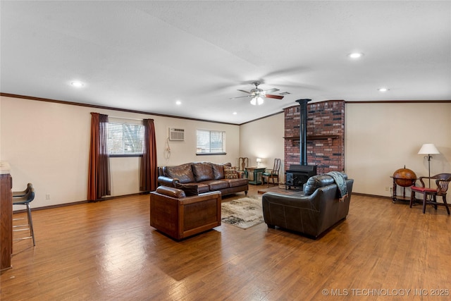 living room featuring hardwood / wood-style floors, a wall unit AC, ornamental molding, ceiling fan, and a wood stove