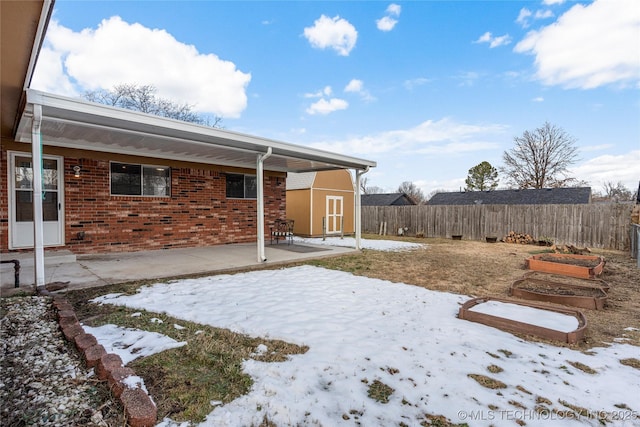 yard covered in snow with a patio and a shed