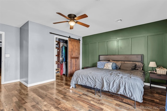 bedroom featuring ceiling fan, a barn door, and dark wood-type flooring