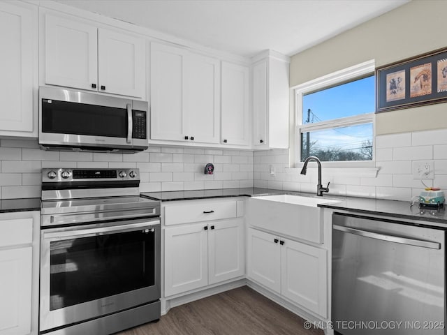 kitchen with decorative backsplash, dark countertops, appliances with stainless steel finishes, and white cabinetry