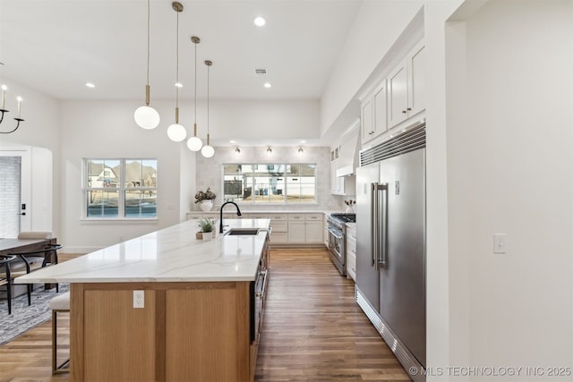 kitchen featuring a center island with sink, sink, white cabinetry, premium appliances, and light stone counters