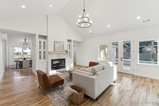 living room featuring an inviting chandelier, light hardwood / wood-style flooring, french doors, and a stone fireplace