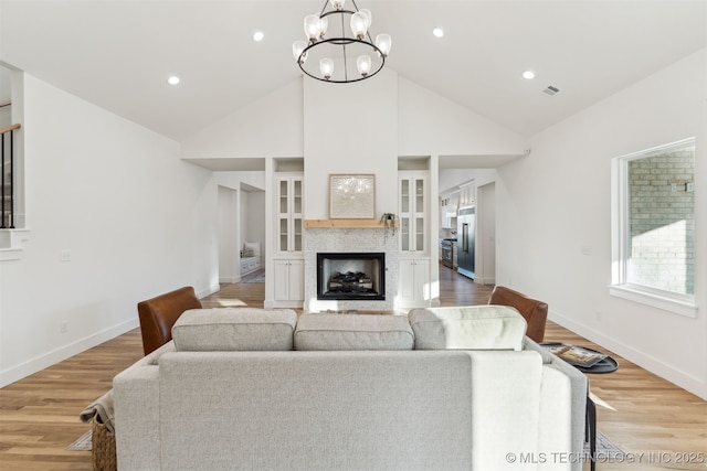 living room with high vaulted ceiling, light wood-type flooring, a stone fireplace, and a chandelier