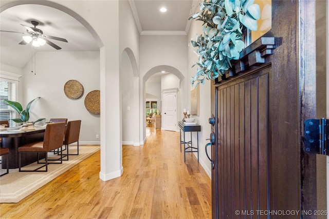 foyer entrance featuring lofted ceiling, ornamental molding, ceiling fan, and light wood-type flooring