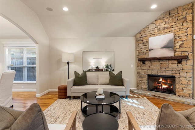 living room featuring lofted ceiling, light hardwood / wood-style floors, and a stone fireplace