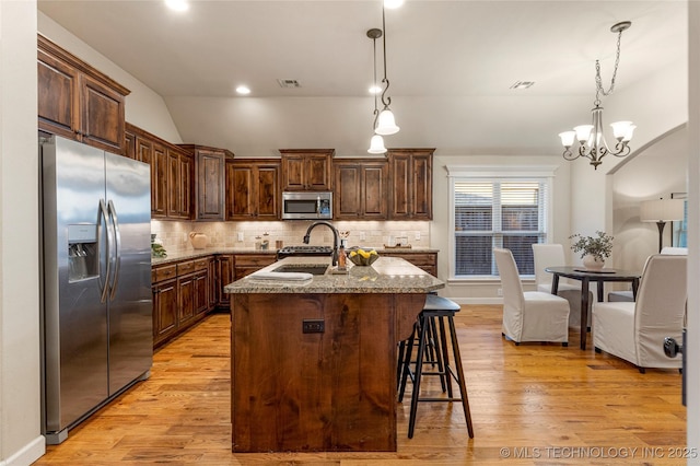 kitchen with a kitchen island with sink, a chandelier, appliances with stainless steel finishes, sink, and decorative light fixtures