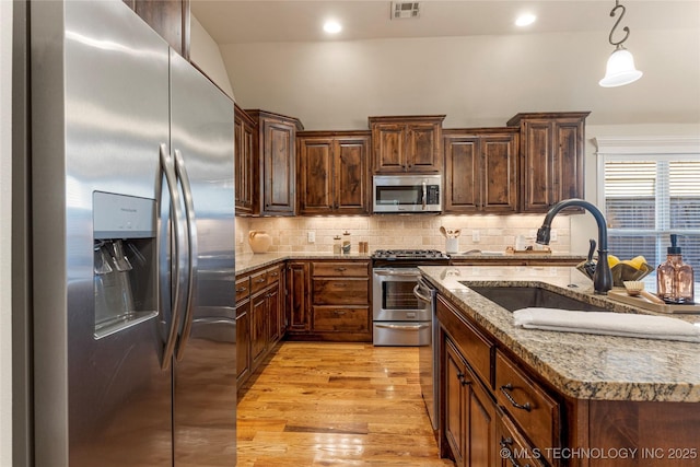 kitchen featuring appliances with stainless steel finishes, pendant lighting, tasteful backsplash, and sink