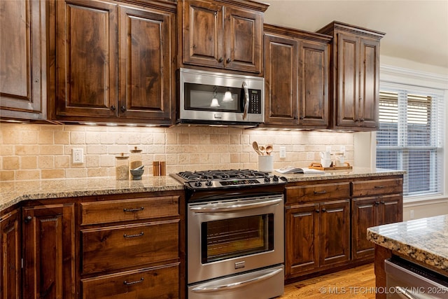 kitchen with light hardwood / wood-style floors, decorative backsplash, dark brown cabinets, light stone countertops, and appliances with stainless steel finishes