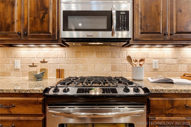 kitchen with light stone countertops, dark brown cabinetry, tasteful backsplash, and appliances with stainless steel finishes