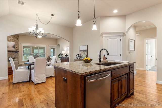 kitchen featuring dishwasher, an island with sink, a notable chandelier, light stone counters, and sink