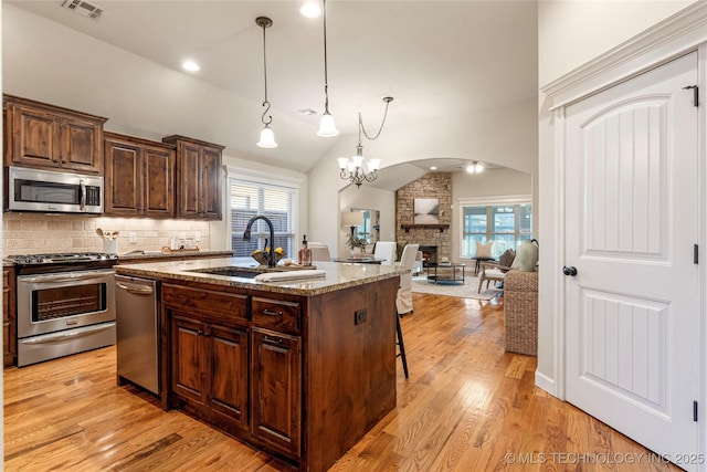 kitchen with a kitchen island with sink, appliances with stainless steel finishes, light stone countertops, decorative light fixtures, and backsplash