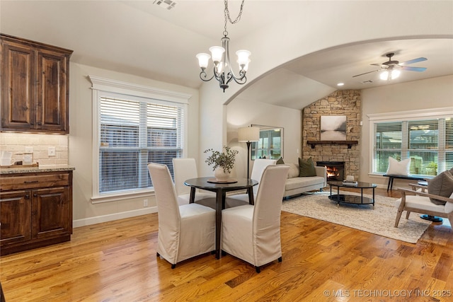 dining space with lofted ceiling, a fireplace, light wood-type flooring, and ceiling fan with notable chandelier