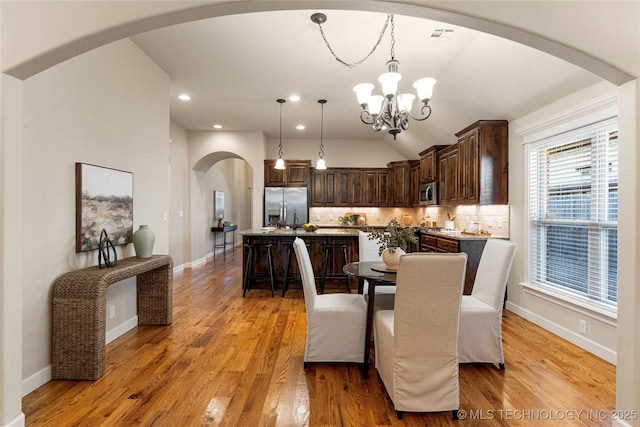 dining area with a healthy amount of sunlight, light wood-type flooring, lofted ceiling, and a chandelier