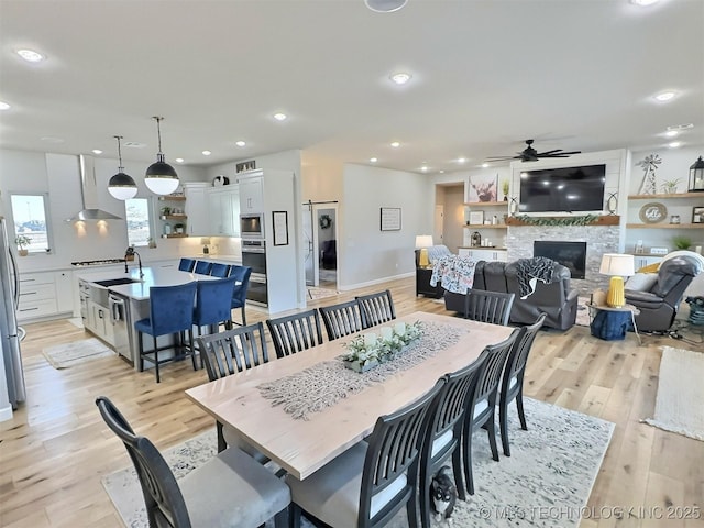 dining room featuring sink, ceiling fan, light hardwood / wood-style floors, and a stone fireplace