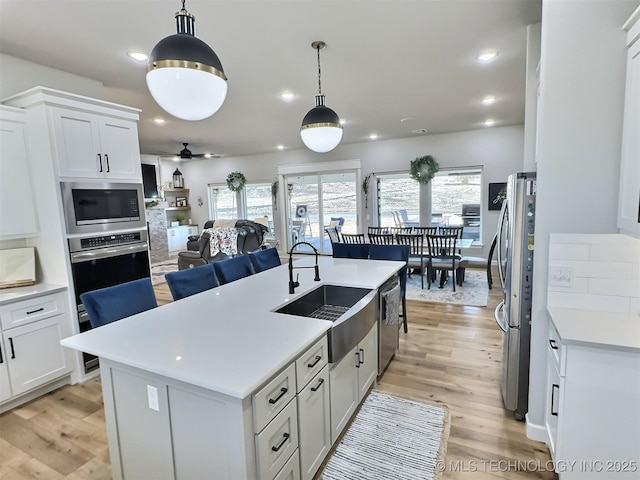 kitchen with sink, stainless steel appliances, white cabinets, and a center island with sink