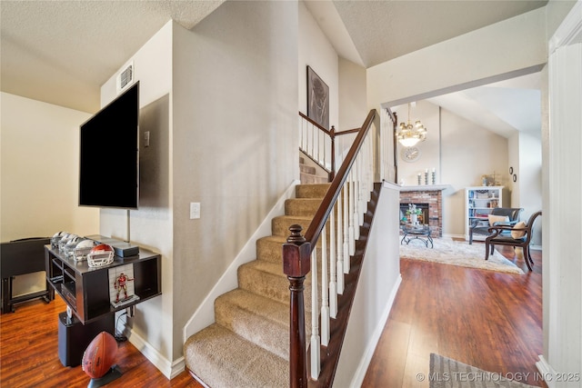 staircase featuring a brick fireplace, a textured ceiling, vaulted ceiling, and wood-type flooring