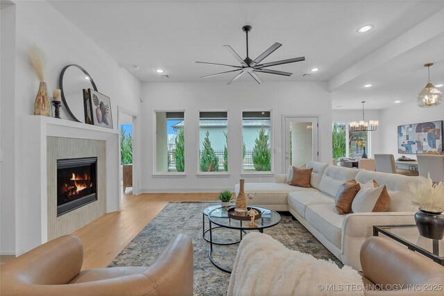 living room featuring a premium fireplace, light wood-type flooring, and ceiling fan with notable chandelier