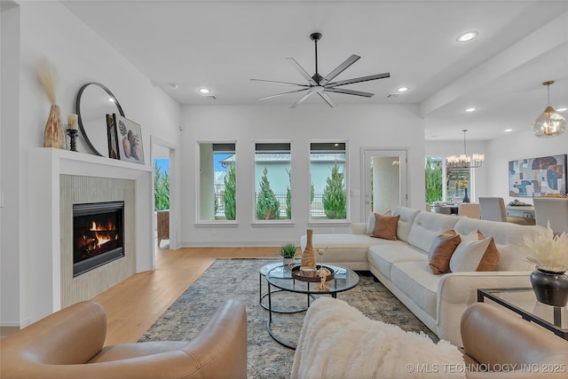 living room with ceiling fan with notable chandelier, a tile fireplace, and light wood-type flooring