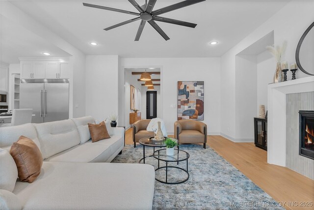 living room with a tile fireplace, light wood-type flooring, and ceiling fan