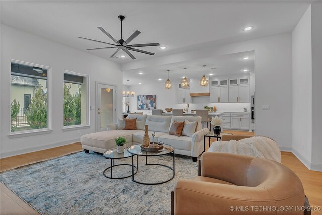 living room with light hardwood / wood-style floors, sink, and ceiling fan with notable chandelier